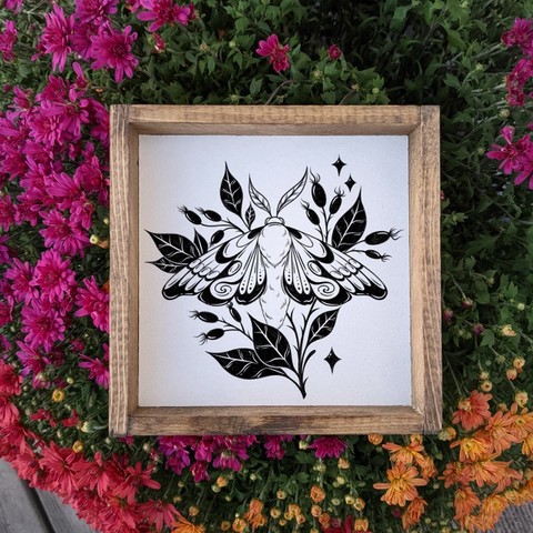 Framed black and white moth illustration on a white background, surrounded by colorful flowers.