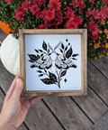 Framed black and white butterfly design held by a hand with flowers in the background