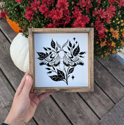 Framed black and white butterfly design held by a hand with flowers in the background