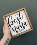 Hand holding a sign with 'Best Nana Ever' text on a dark background