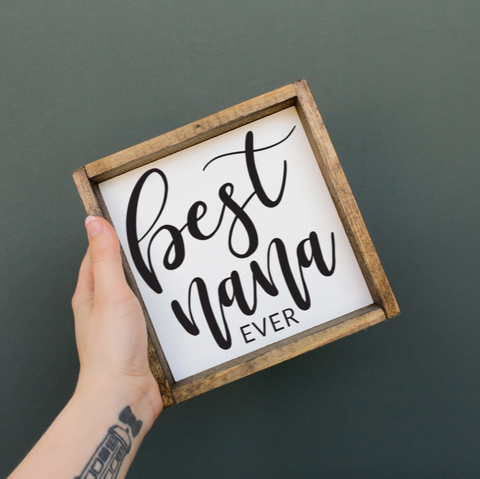 Hand holding a sign with 'Best Nana Ever' text on a dark background