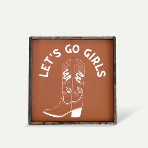 Decorative sign with cowboy boots and 'Let's Go Girls' text on a brown background