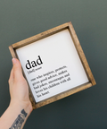 Hand holding a framed definition of 'dad' against a dark background