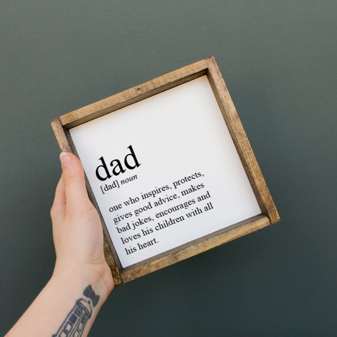 Hand holding a framed definition of 'dad' against a dark background