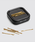 Gold hairpins in a black 'kit-sch' container on a light gray background