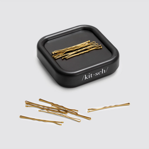 Gold hairpins in a black 'kit-sch' container on a light gray background