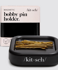 Black bobby pin holder with gold pins and 'kitsch' packaging on a light gray background