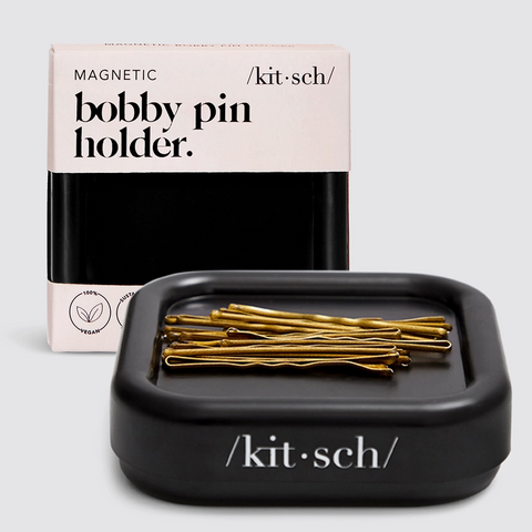 Black bobby pin holder with gold pins and 'kitsch' packaging on a light gray background