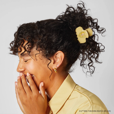 Woman with styled hair wearing a yellow bow and shirt against a light gray background