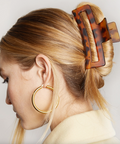 Person with a tortoiseshell hair clip in their blonde hair, wearing gold hoop earrings.