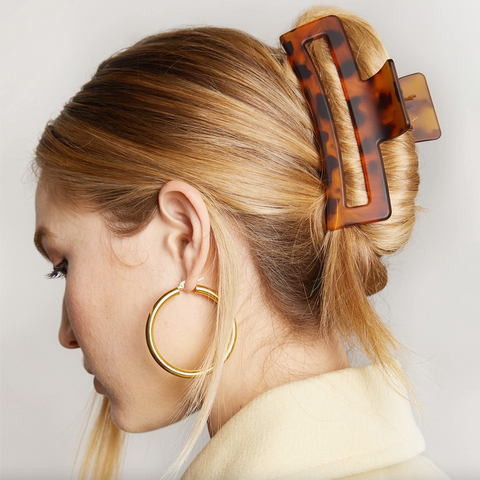 Person with a tortoiseshell hair clip in their blonde hair, wearing gold hoop earrings.