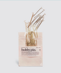 Set of bobby pins in a clear plastic bag with a beige label on a light blue background
