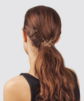 Woman with long brown hair styled in a ponytail with decorative hairpins on a light gray background