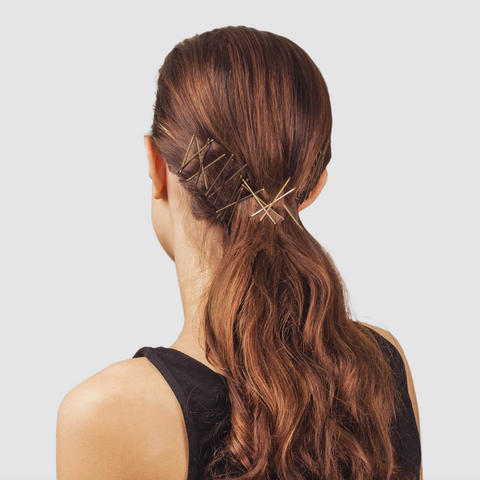 Woman with long brown hair styled in a ponytail with decorative hairpins on a light gray background