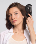 Woman brushing her hair with a black brush against a light gray background