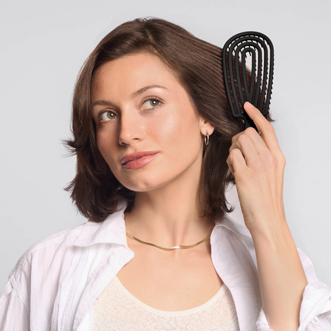Woman brushing her hair with a black brush against a light gray background