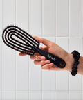 Person holding a black hairbrush with a white tiled wall background