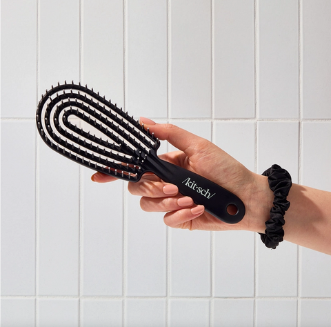 Person holding a black hairbrush with a white tiled wall background