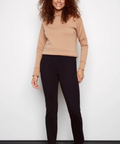Woman wearing a beige sweater and black pants against a white background