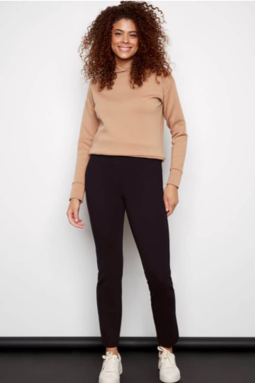 Woman wearing a beige sweater and black pants against a white background