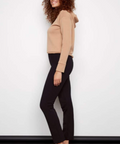 Woman wearing a beige sweater and black pants against a white background