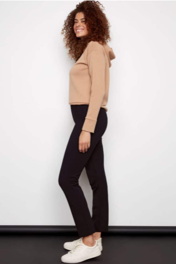Woman wearing a beige sweater and black pants against a white background