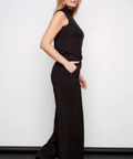 Woman wearing a black sleeveless top and high-waisted pants against a white background