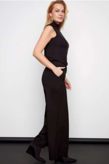 Woman wearing a black sleeveless top and high-waisted pants against a white background
