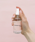 Hand holding a bottle of coconut milk with a pink background