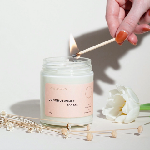 Candle being lit with a match, surrounded by flowers and dried plants on a light background