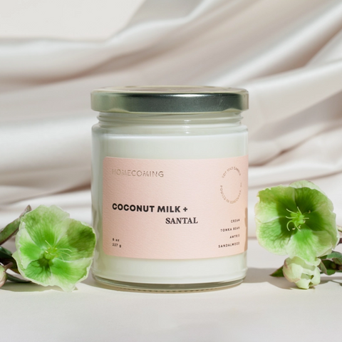 Candle labeled 'Coconut Milk + Santal' with green flowers on a light background