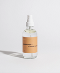 Clear spray bottle with a brown label on a light gray background