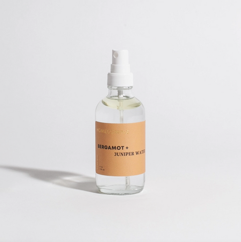 Clear spray bottle with a brown label on a light gray background