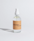 Clear spray bottle with a brown label on a light gray background