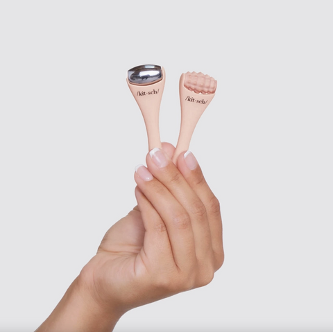 Hand holding two small skincare devices with 'skin' branding against a light background