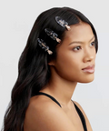 Woman with long dark hair wearing decorative hair clips on a light gray background