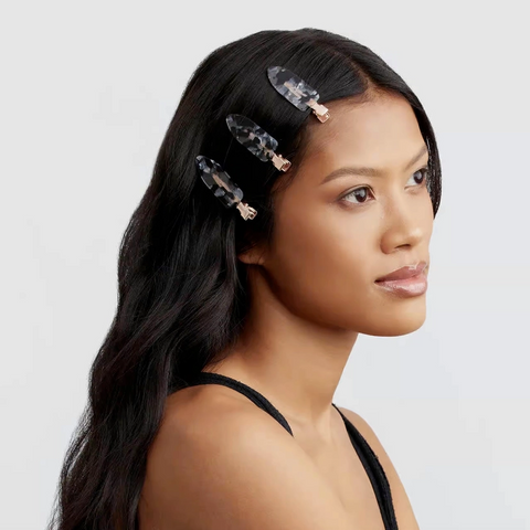 Woman with long dark hair wearing decorative hair clips on a light gray background