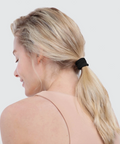 Woman with blonde hair tied in a ponytail with a black hair tie on a white background