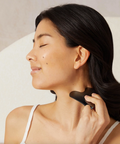 Woman using a black skin care tool on her neck against a neutral background