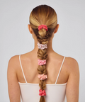 Woman with braided hair wearing pink scrunchies on a plain background