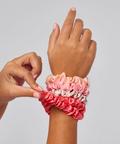 Hand wearing a colorful scrunchie with another hand adjusting it on a plain background