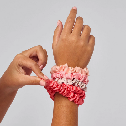 Hand wearing a colorful scrunchie with another hand adjusting it on a plain background