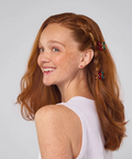 Woman with red hair styled in a ponytail with decorative clips against a plain background