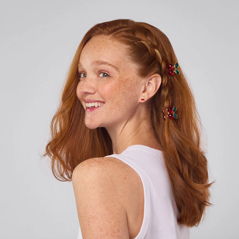 Woman with red hair styled in a ponytail with decorative clips against a plain background