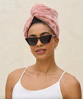 Woman wearing a pink towel on her head and sunglasses with a beige background