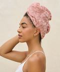 Woman wearing a pink towel on her head against a beige background