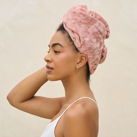 Woman wearing a pink towel on her head against a beige background