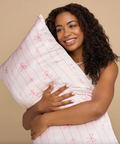 Woman holding a white pillow with pink patterns against a beige background