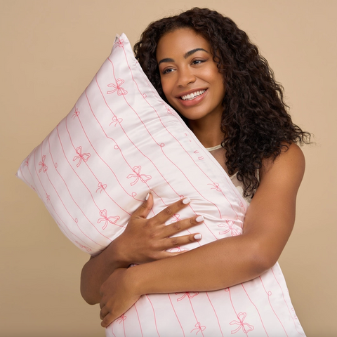 Woman holding a white pillow with pink patterns against a beige background