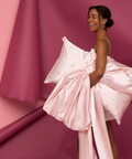 Woman in a pink dress with a large bow against a pink background